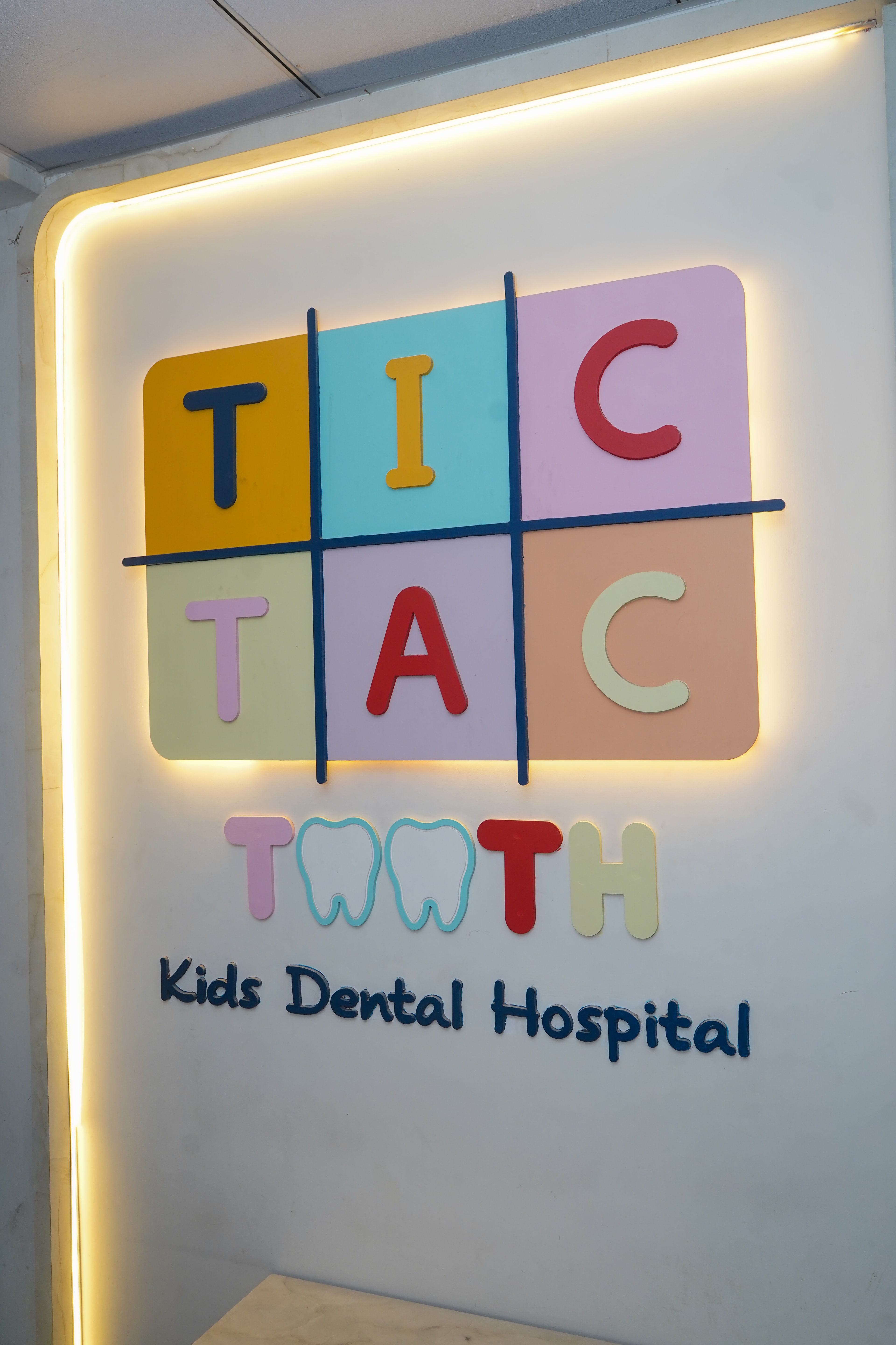 The Tic Tac Tooth Kids Dental Hospital entrance sign, dimensional pastel letters on a noughts-and-crosses grid, edge-lit in warm gold