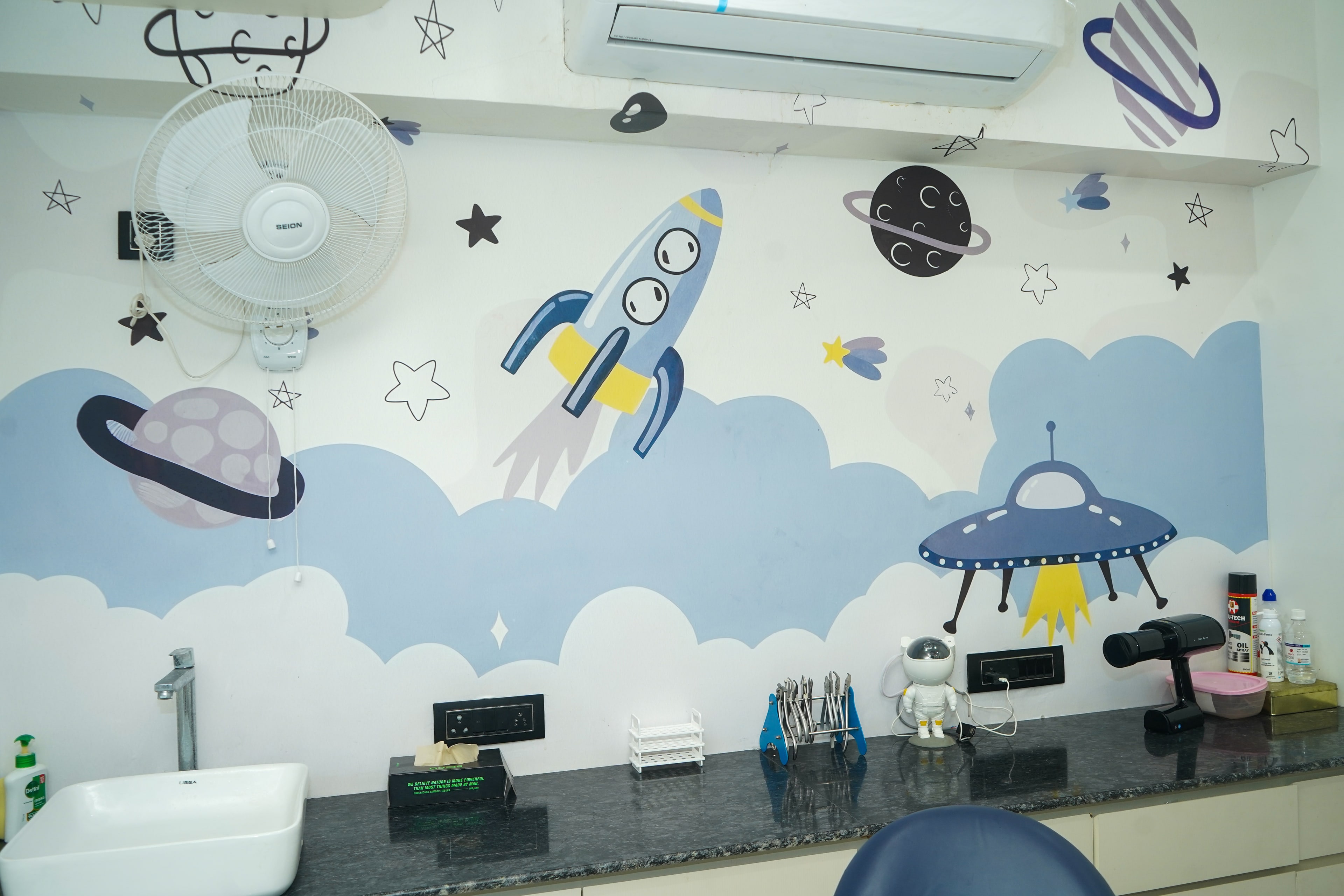 The space room mural, a blue rocket, a UFO and ringed planets over a pale blue cloudscape, above the granite counter and sink